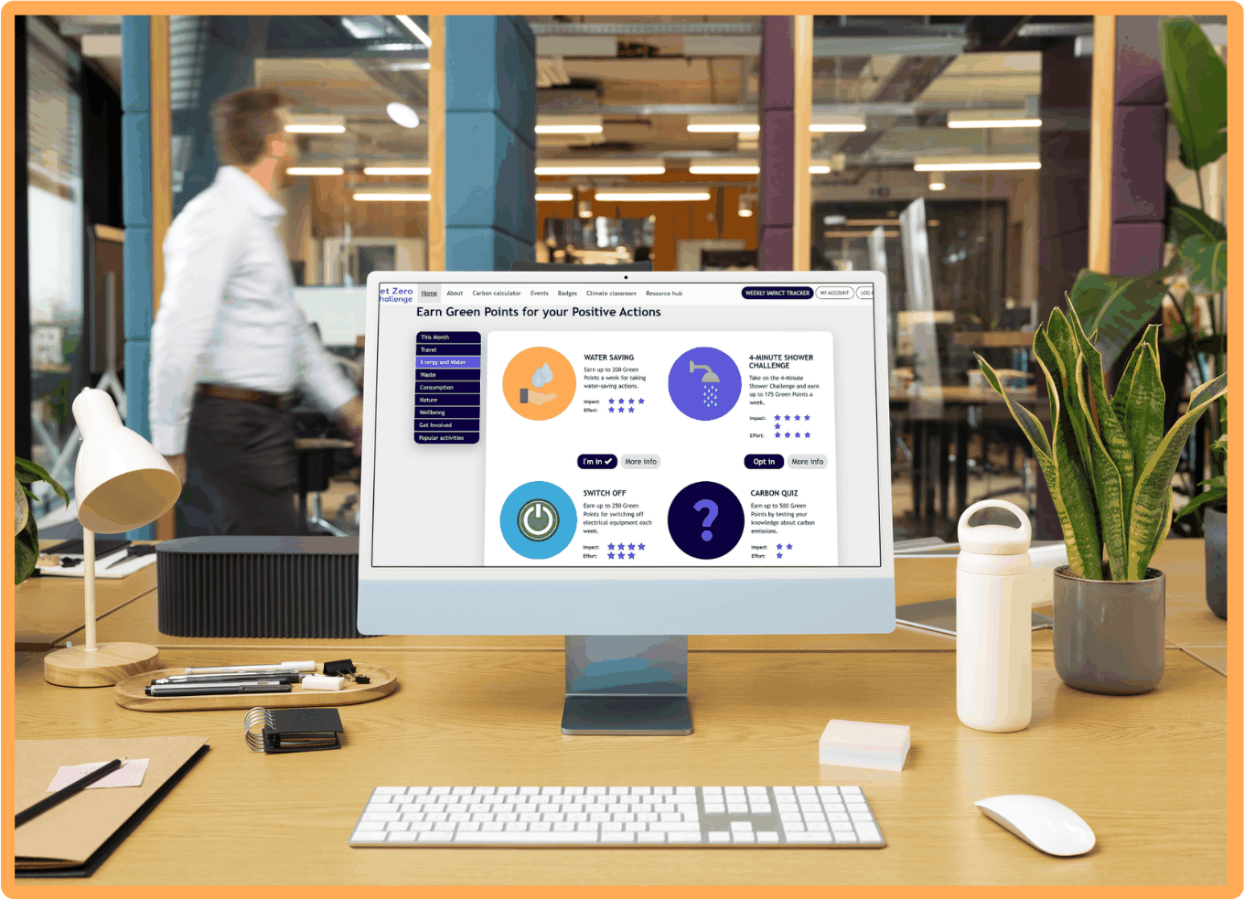 A desktop monitor on an office desk showing the Climate Action Challenge web dashboard, with a colleague walking past in the background